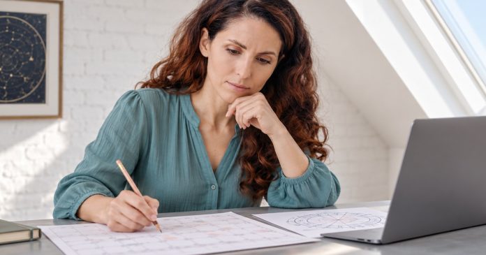 Mercury Retrograde Dates 2026–2030 A woman marking a printed planner beside an astrology chart and a graphite laptop.